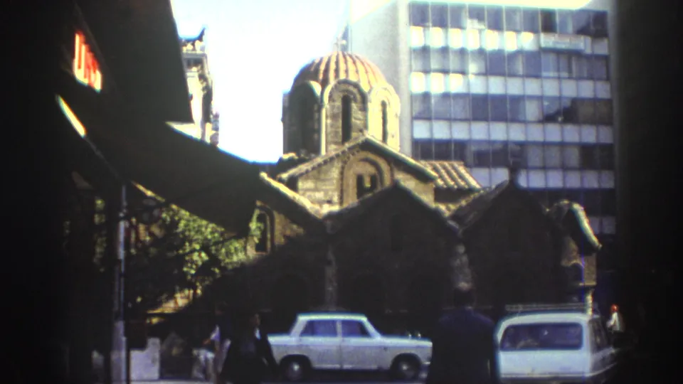 A domed historic church-like building in Tel Aviv appears near modern glass buildings, awnings, pedestrians, and parked older cars.