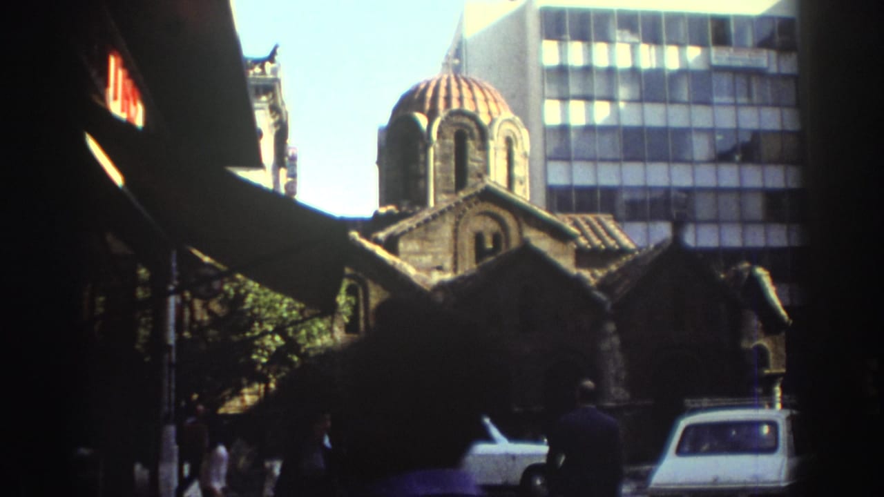 Historic stone church with a red dome seen between shaded street edges and a modern building.