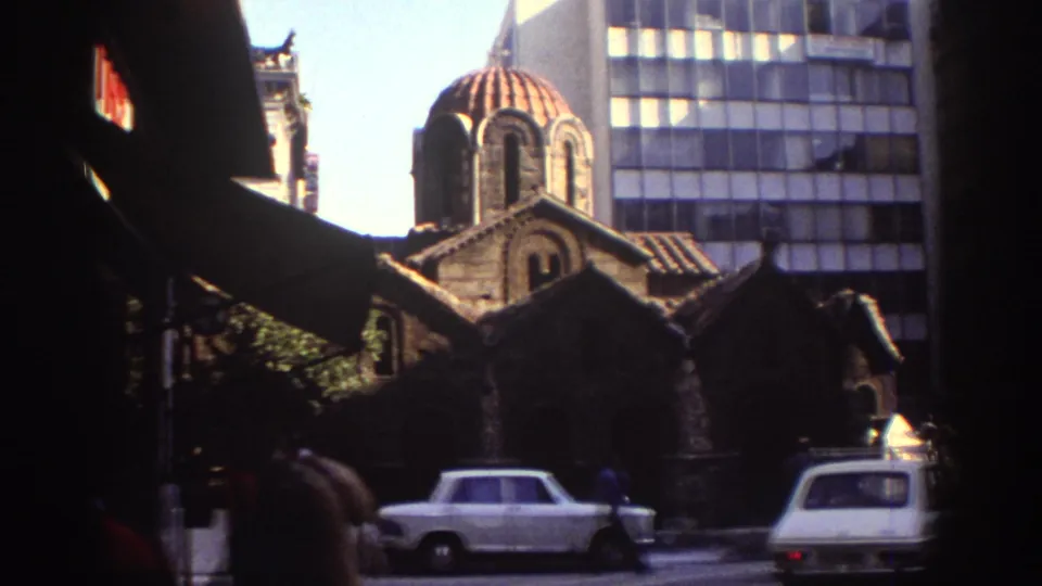1976 Tel Aviv street scene with white period cars, pedestrians, shaded overhangs, and a historic red-domed church against modern buildings.
