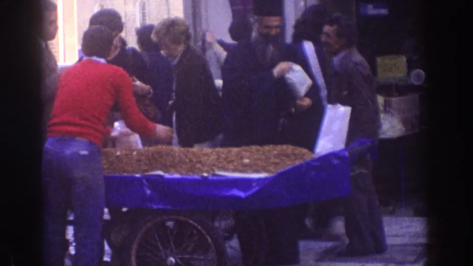 1976 Tel Aviv street scene with adults around a blue-covered roasted nut cart, including a man in dark religious dress.