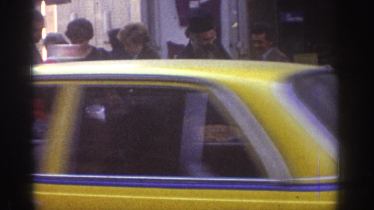 A yellow taxi crosses the foreground while the Tel Aviv nut vendor scene continues behind it in soft 8mm focus.