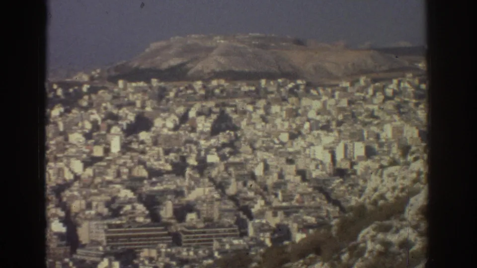 Wide 1976 Tel Aviv city view with dense urban buildings and distant low hills under hazy 8mm color.