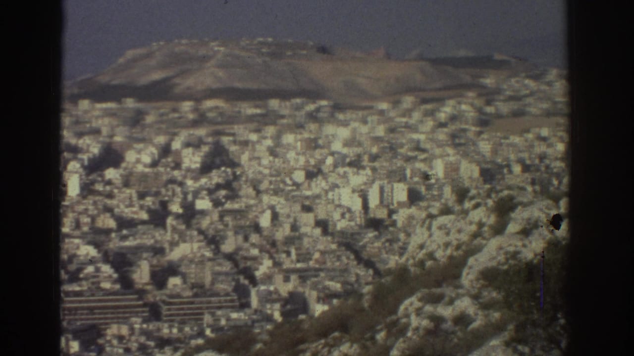 1976 Tel Aviv hilltop view showing dense pale buildings beyond rocky foreground terrain under a hazy sky.