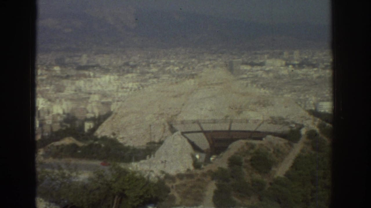City panorama with rocky slope, trees, distant buildings, and film gate edges.