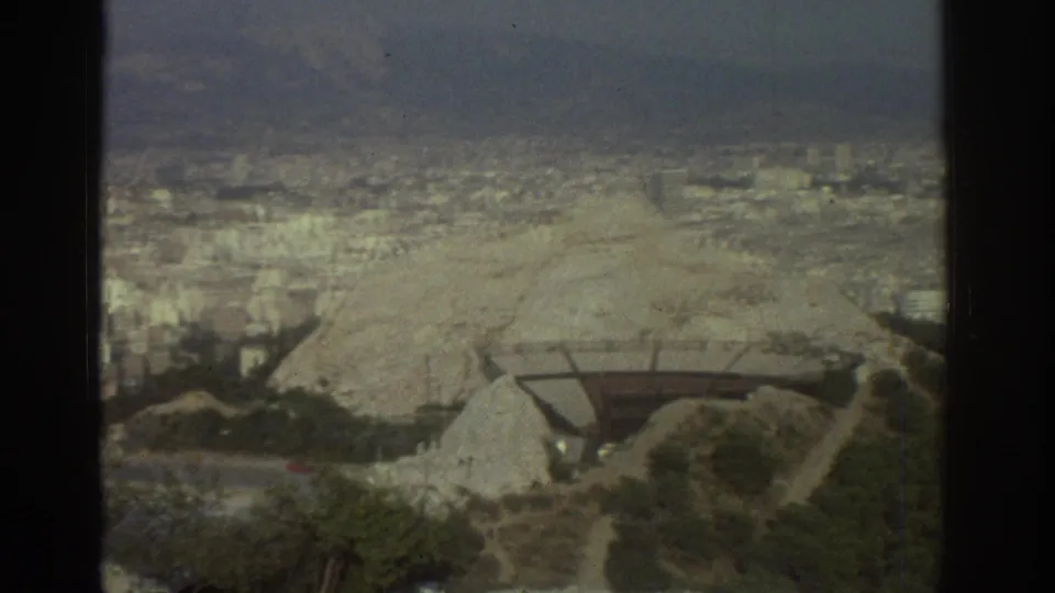 1976 Tel Aviv frame from an elevated lookout, with a pale hillside in front of dense urban development and distant terrain.