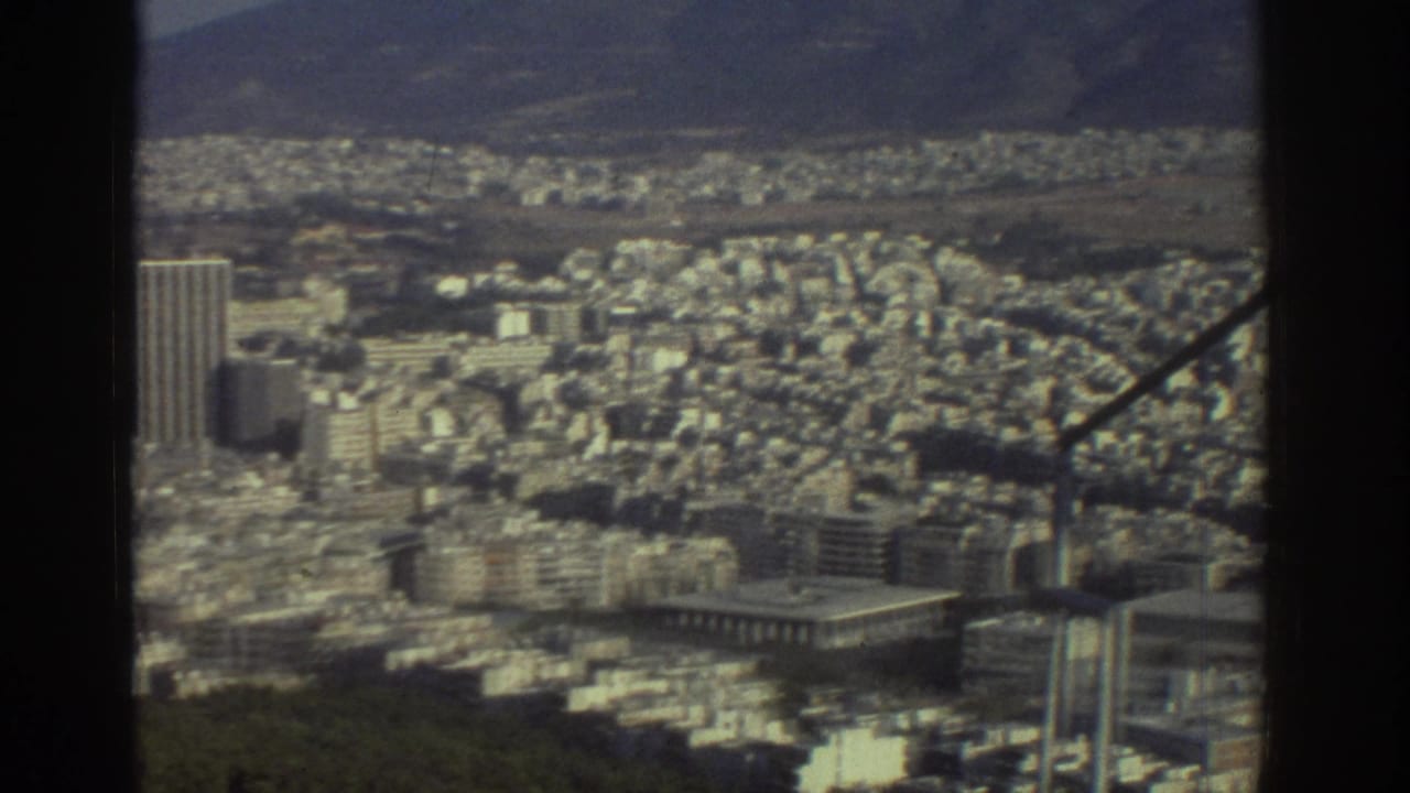 1976 Tel Aviv elevated view showing dense pale buildings, a taller tower, distant hills, and dark structural framing in the foreground.