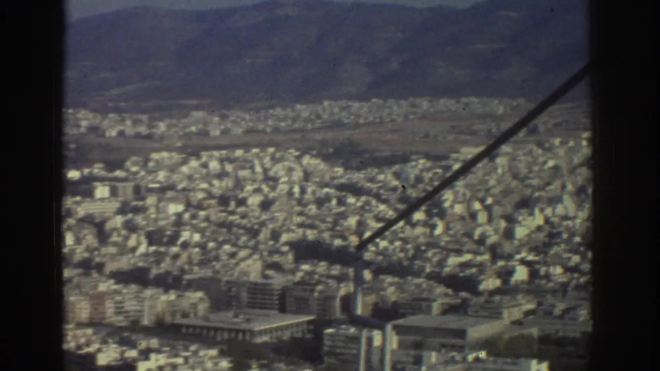 Elevated 1976 Tel Aviv city view with compact apartment blocks, distant hills, and a diagonal support beam in the foreground.