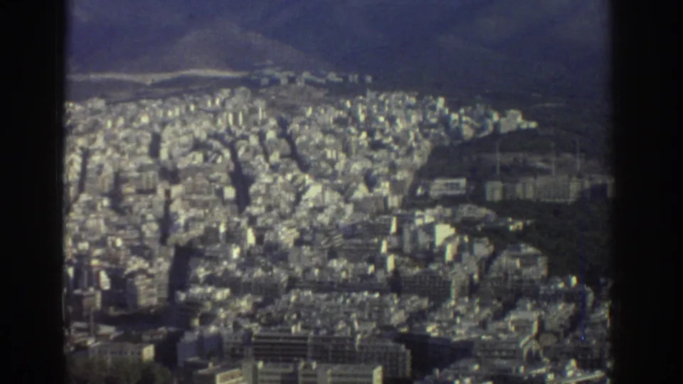 Wide 1976 Tel Aviv view from an elevated position, showing dense urban blocks, distant hills, and dark foreground posts or supports.