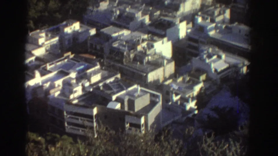 Final 1976 Tel Aviv frame showing flat-roofed residential structures, sunlit walls, and greenery through soft 8mm texture.