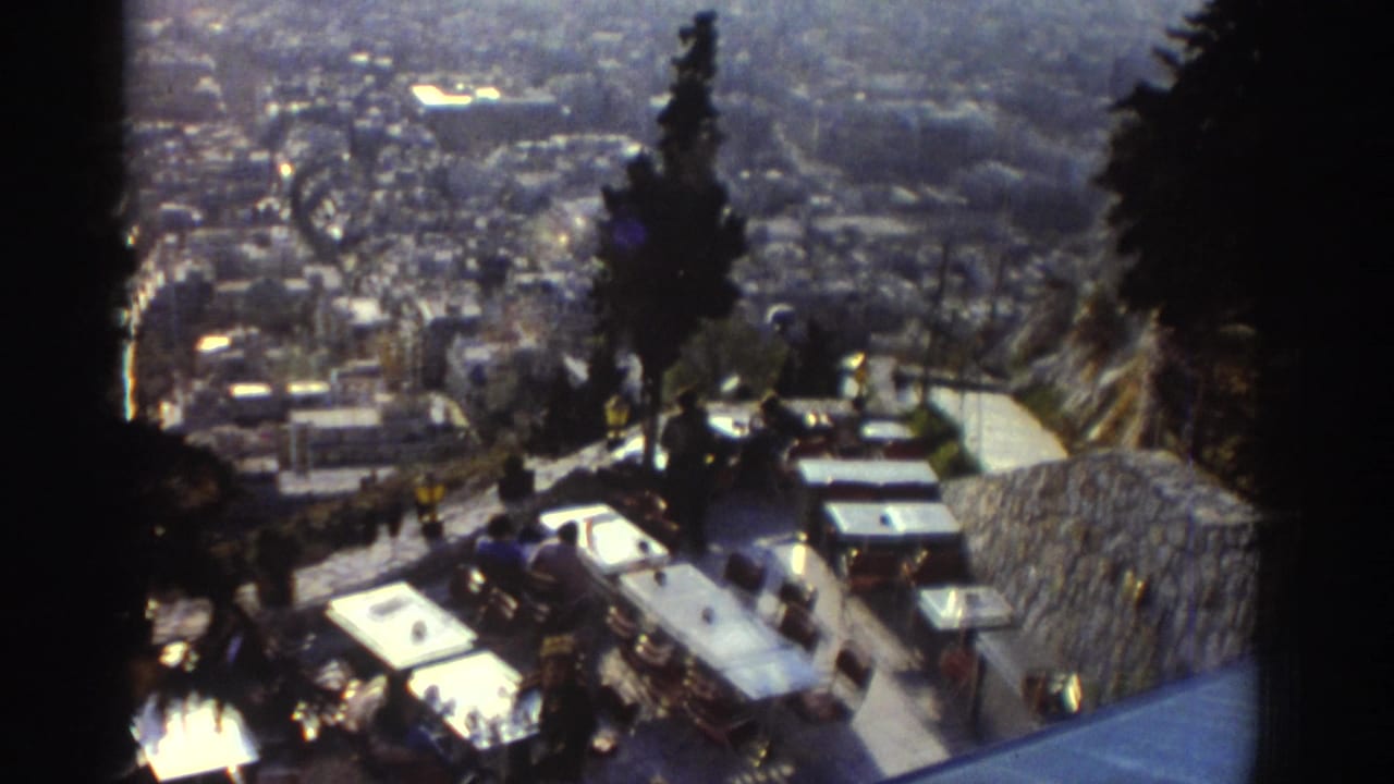 1976 Israel home-movie frame showing an outdoor terrace and parked cars above a dense city view.