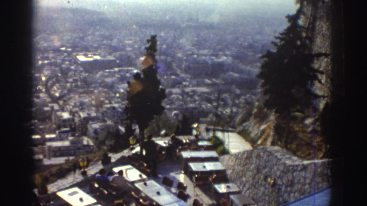 1976 Israel travel frame with terrace seating, a curving stone wall, trees, and a distant urban panorama.