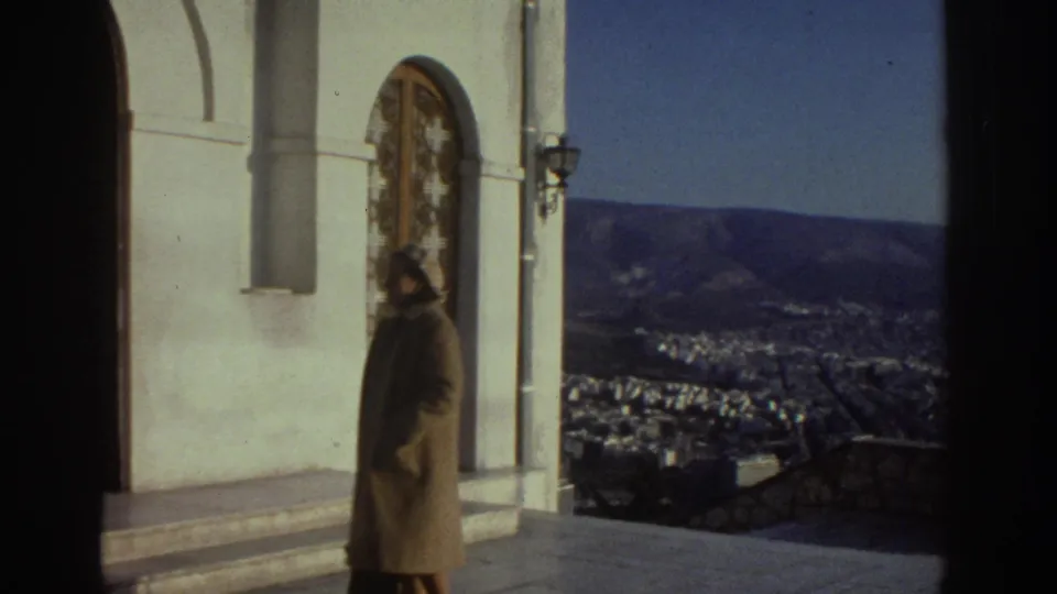 1976 Israel travel frame of a woman near a church entrance, with mountains and city buildings visible behind her.