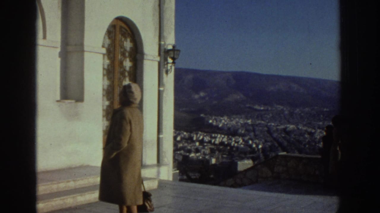 1976 Israel home-movie frame showing a woman in a coat and headscarf near an arched church doorway with a city and hills below.
