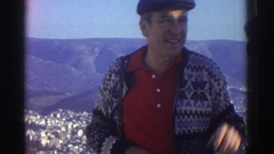 1976 Israel home-movie frame showing a smiling male visitor in a patterned sweater at a high overlook above the city.