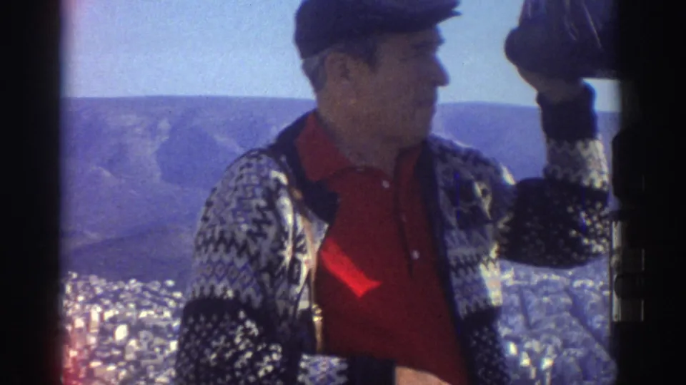1976 Israel travel frame showing a man in a cap lifting a camera at a hilltop viewpoint above the city.