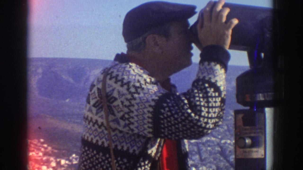 Man looks through a public binocular viewer with hills and city below.