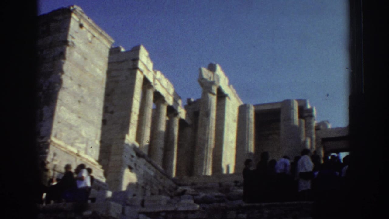 Tourists stand near pale stone pillars and stepped ruins under a blue sky.