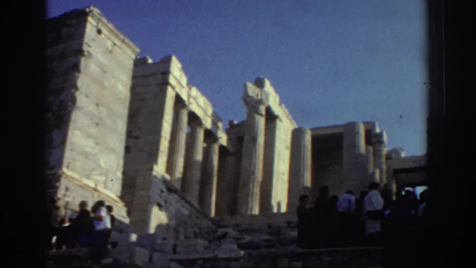 1976 8mm frame from Israel showing visitors gathered beside pale stone pillars and weathered ruins under clear sky.