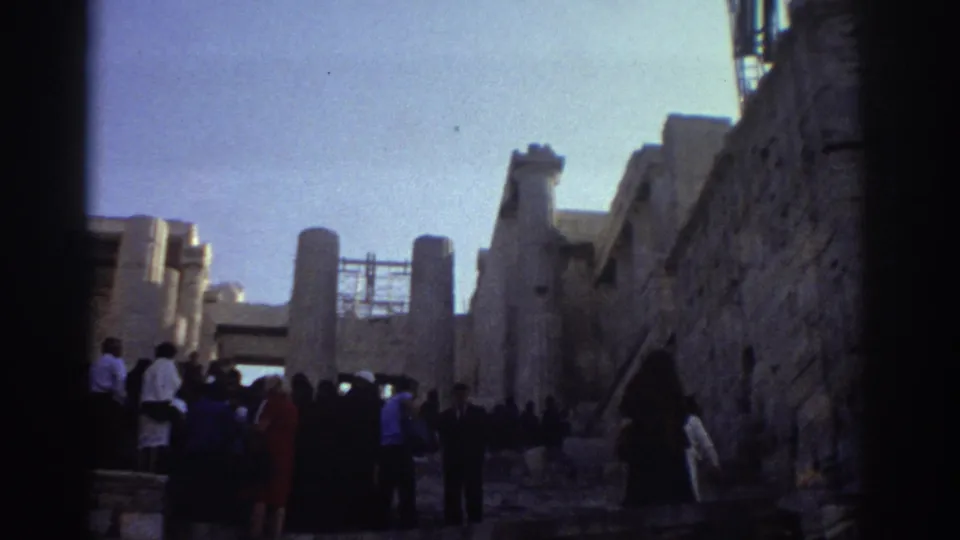 1976 Israel 8mm frame showing visitors in period clothing beside tall stone walls, pillars, and rough masonry under bright sky.