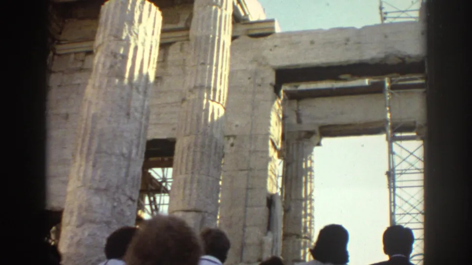 1970s 8mm travel frame showing visitors at the base of fluted stone columns with scaffolding visible through openings.