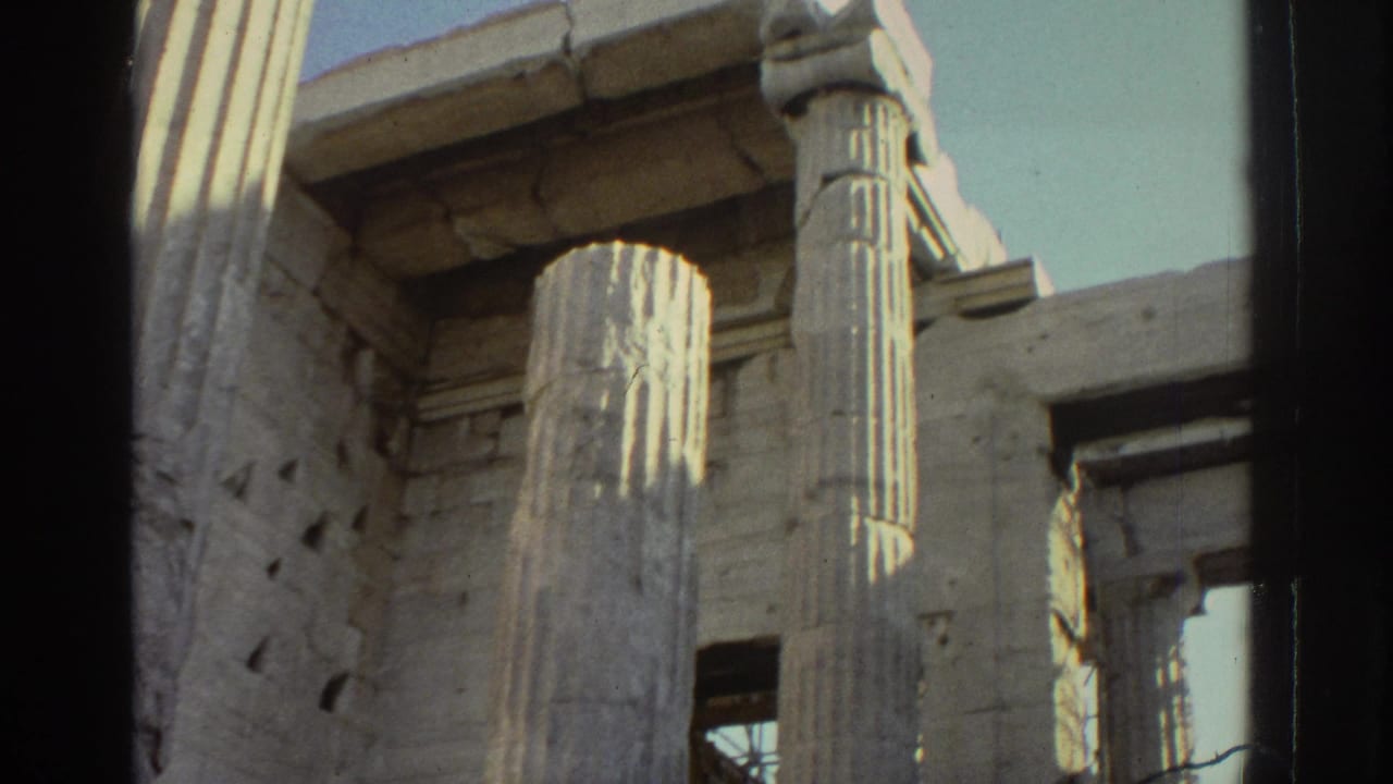 Weathered fluted columns and rectangular stone openings fill the frame, with scaffolding behind the ruin and a dark film border at left.