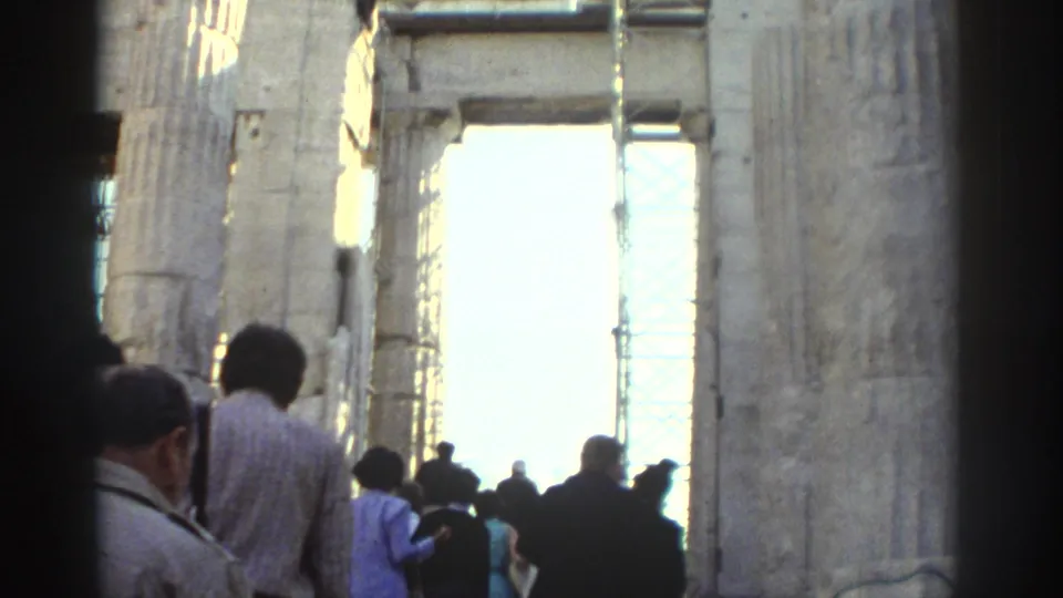 1970s 8mm travel footage shows visitors moving through tall weathered stone ruins with a bright exterior opening ahead.