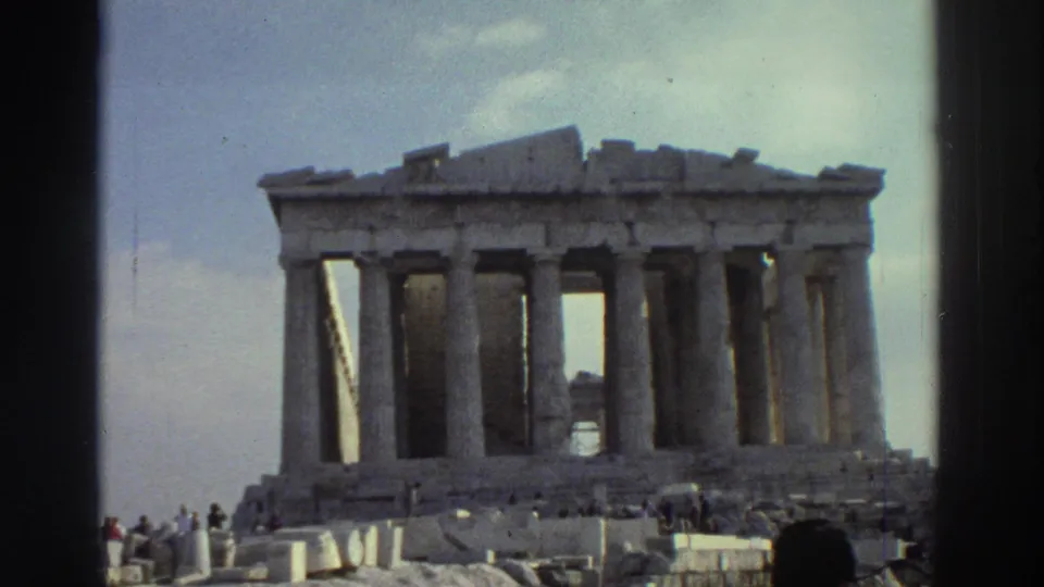 Handheld 8mm footage frames a columned ruin with visitors at the base and dark gate edges visible on both sides.