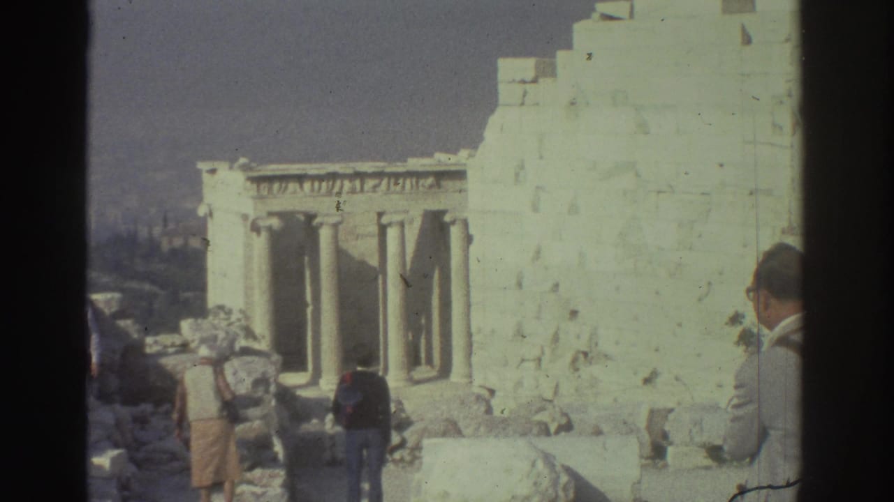 Tourists stand among pale stone columns and broken ruins under open sky.