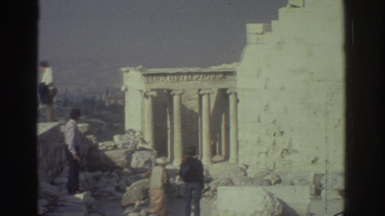 Visitors walk and stand beside stone ruins with columns in the background.