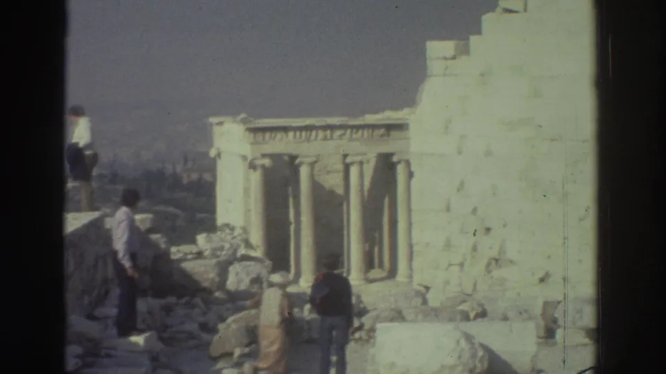 1976 tourist footage frame with several visitors moving around ancient stonework and columned ruins.