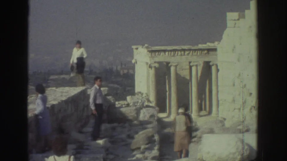 1976 home-movie frame showing tourists walking along ancient stonework near columned ruins.