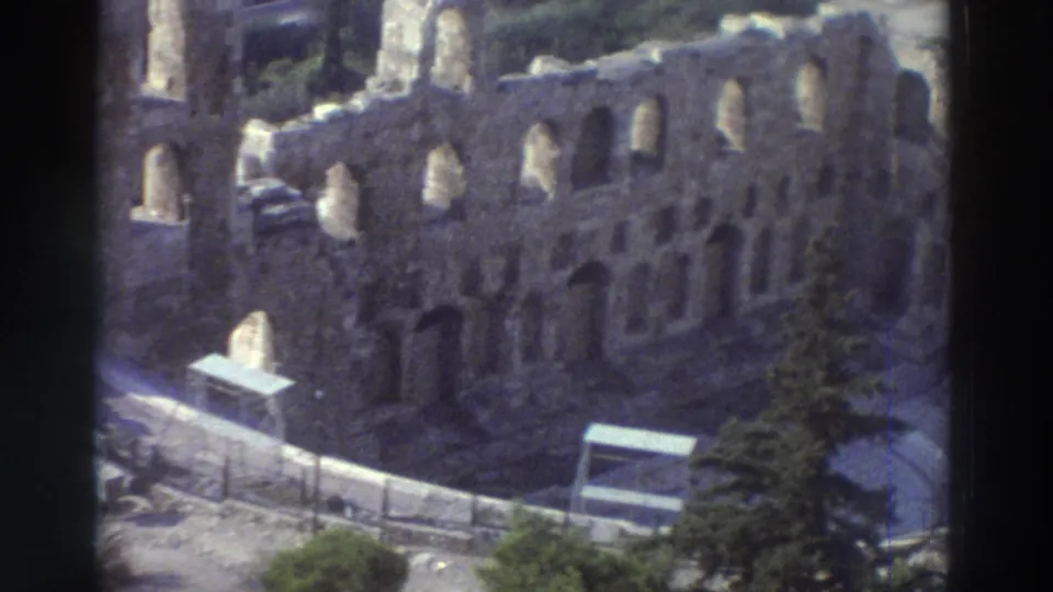 1976 8mm travel frame showing a closer elevated view of the Odeon stone wall, arched openings, railing, path, trees, and small structures at the base.