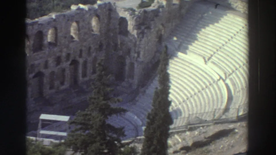 1976 8mm frame from Tel Aviv, Israel, with pale curved seating, arched ruin walls, trees, and visible film gate borders.