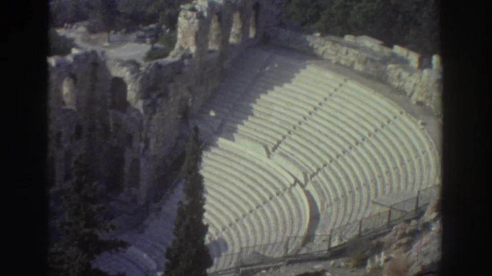 Sunlit 1976 8mm view in Tel Aviv, Israel, showing broad curved seating, ruin walls, railings, and tall cypress trees.