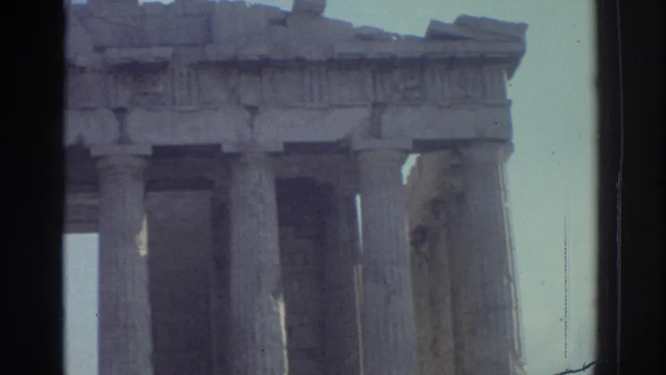 1970s 8mm travel frame showing classical temple columns and broken upper stonework, with dark film edges visible.