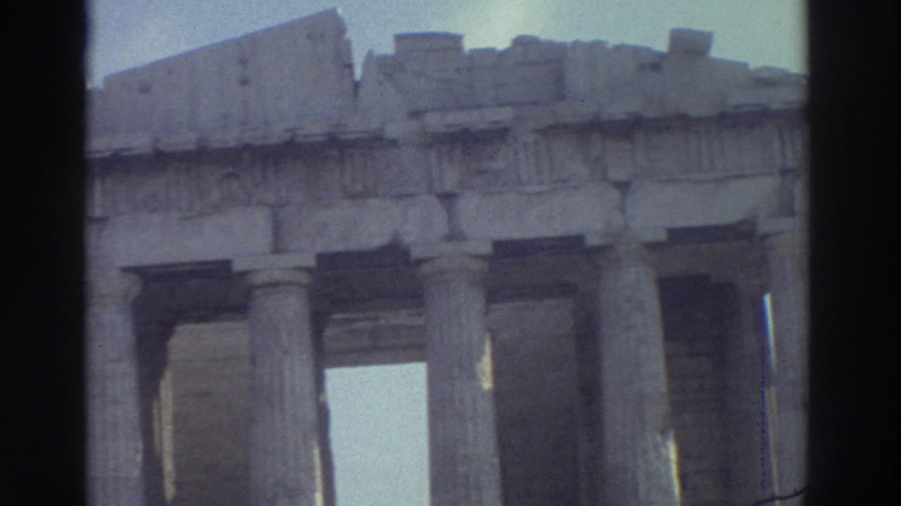 Home-movie frame of a classical ruin facade, showing columns, weathered masonry and a pale sky through the openings.