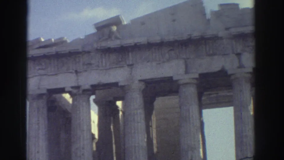 1970s 8mm frame with a tilted visitor view of classical columns, broken entablature and sunlit stone surfaces.