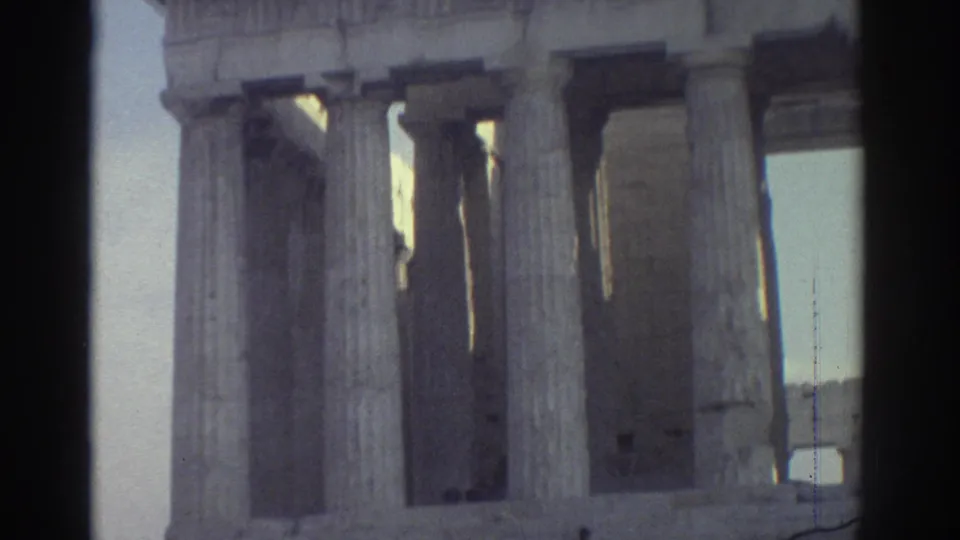 1970s 8mm travel frame showing tall classical columns and a small distant visitor at the base of the ruins.
