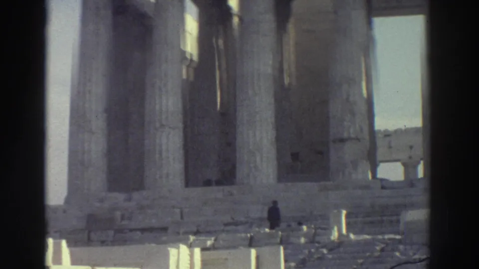 1976 8mm frame of ancient stone columns and ruins in Israel, with a small visitor figure walking among the pale masonry.