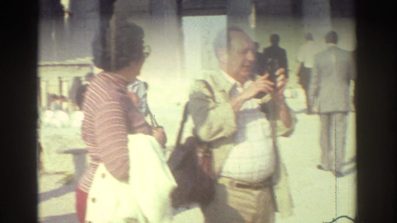 Tourists at an ancient site in Israel, including a man handling a camera beside a woman in a striped top and red pants.