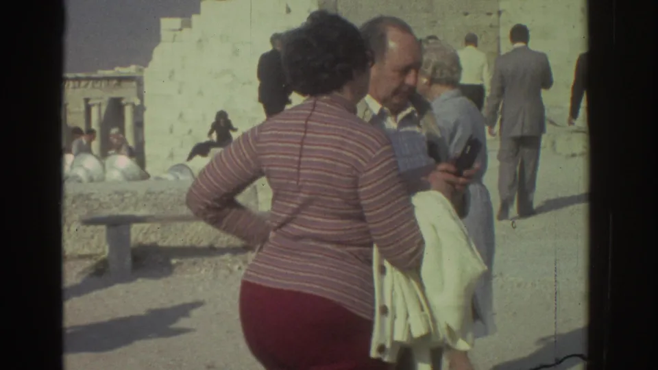 Tourist group at ancient ruins in Israel, with a woman in a striped sweater foregrounded and a man holding a camera beside her.