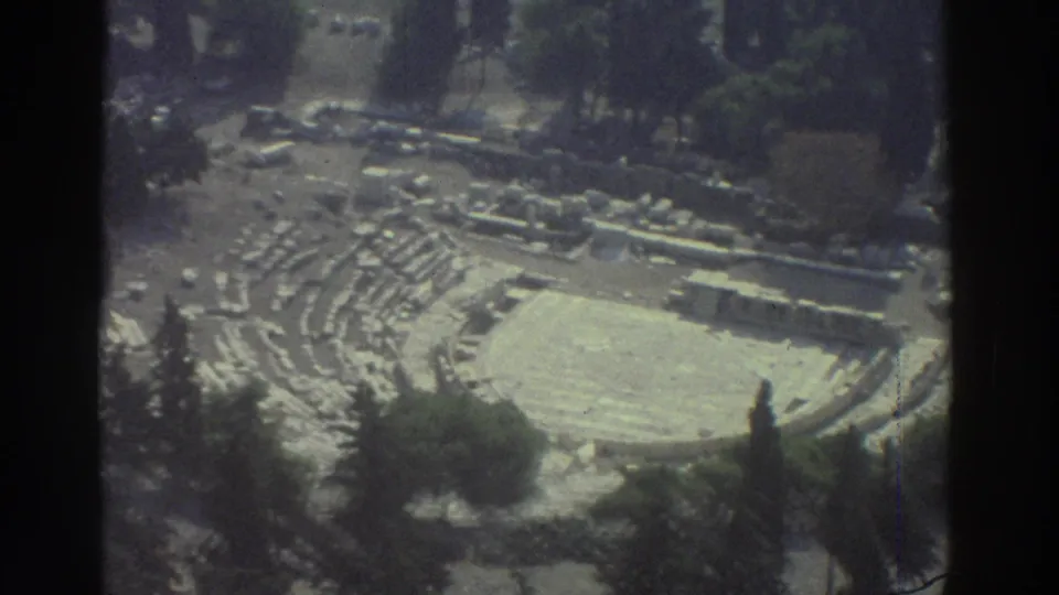 The 1976 home-movie view looks down on curved stone seating and an open arena, with trees partly obscuring the lower edge.