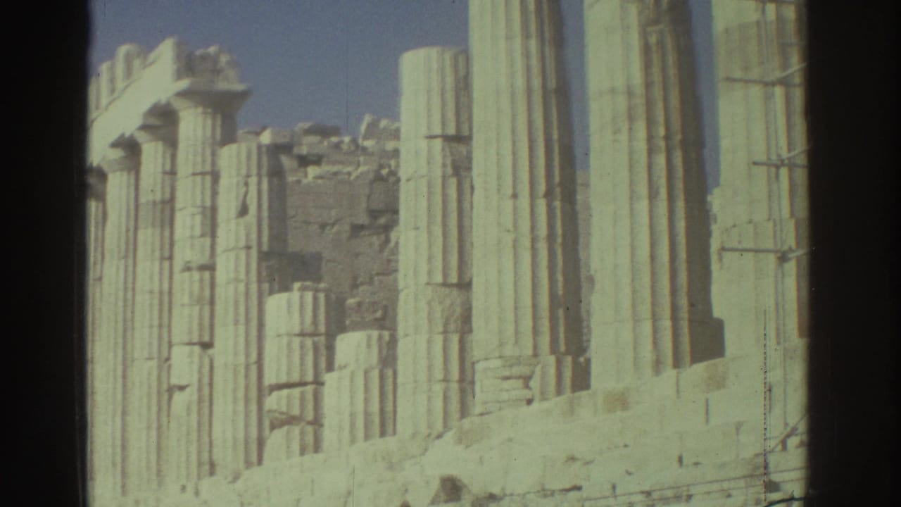 Pale columns and scaffolding seen beside weathered stone ruins under a clear sky.