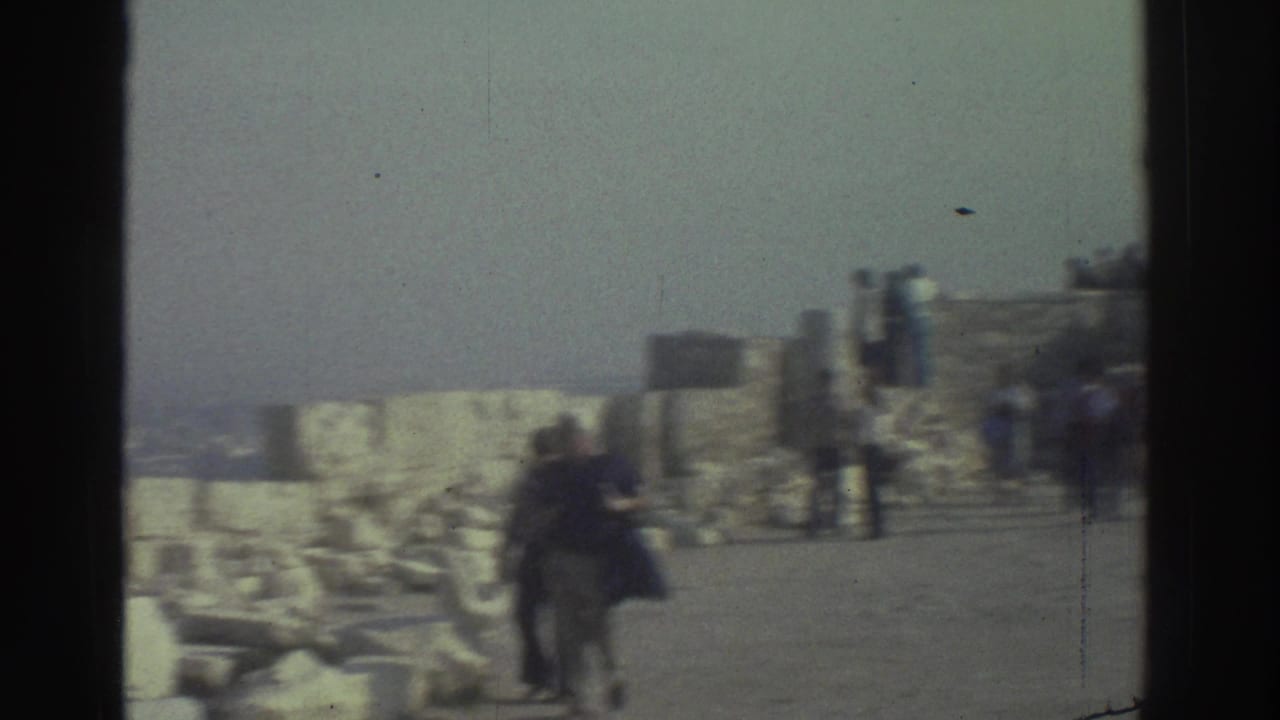 Tourists walk along a stone path beside low walls and rubble.