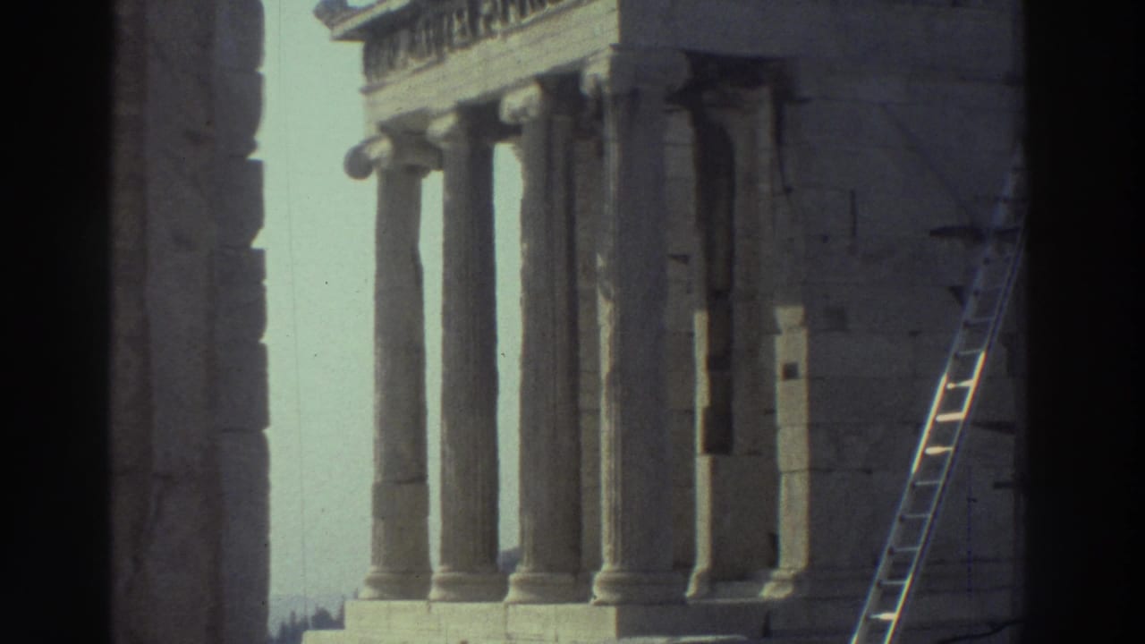 1970s 8mm travel frame showing classical stone columns, block masonry, and a ladder near a weathered ruin under pale sky.