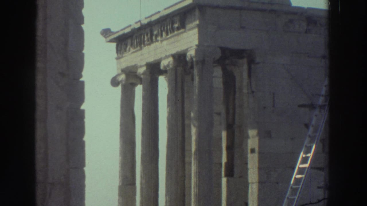 Similar view of columns, stone wall, and a ladder near a ruin with dark film borders.