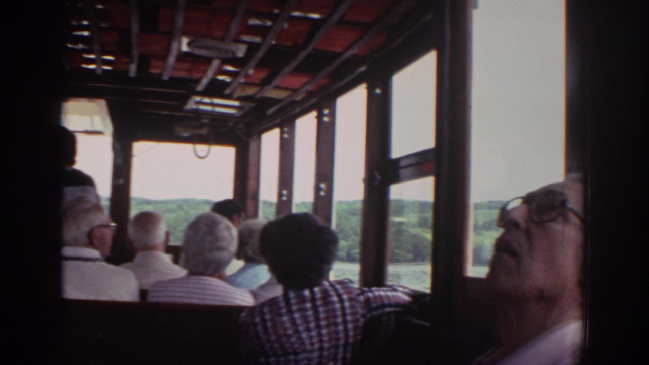 1976 Watkins Glen tour boat passengers sit inside a wooden cabin while looking toward the lake and wooded shoreline outside.
