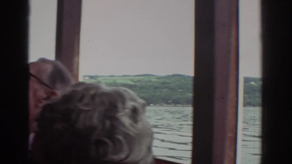 Inside the Watkins Glen tour boat cabin, passengers sit close to the windows as the lake and tree-covered shore appear outside.