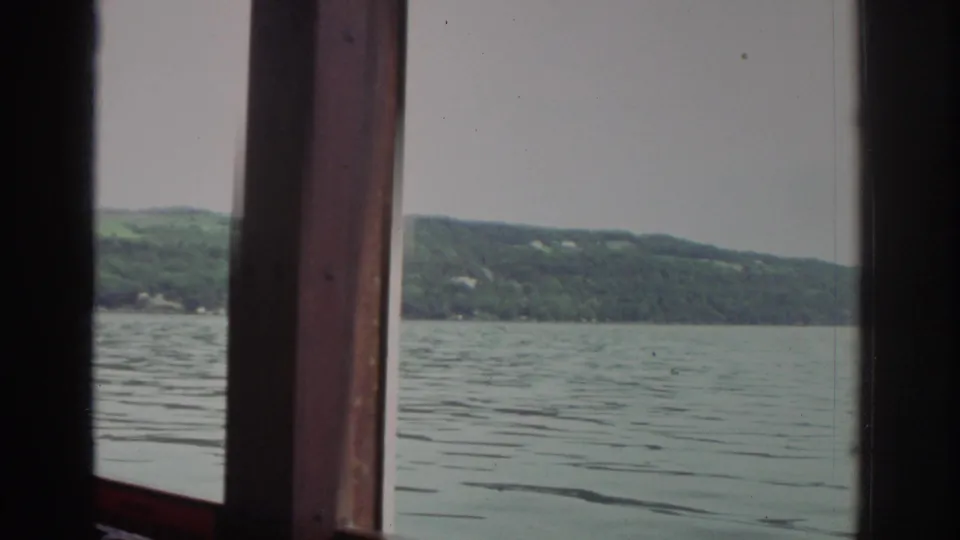 The view from the 1976 Watkins Glen tour boat shows calm lake water and wooded hills through the cabin's wooden windows.