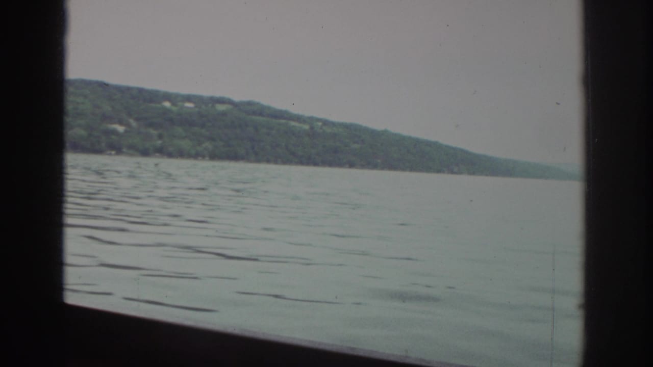 Wide lake surface with ripples and a tree-covered shoreline beyond a dark window frame.